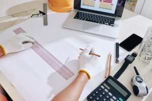 Construction engineer drawing blueprint of house and checking scheme on laptop screen
